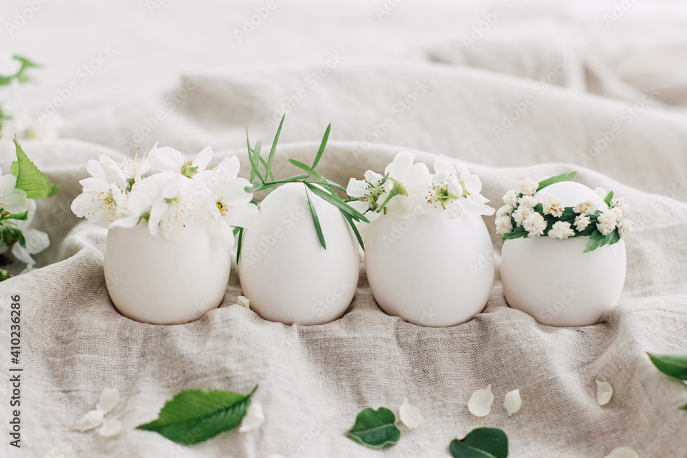 Natural easter eggs in cute floral wreaths on linen fabric with blooming spring branch and petals