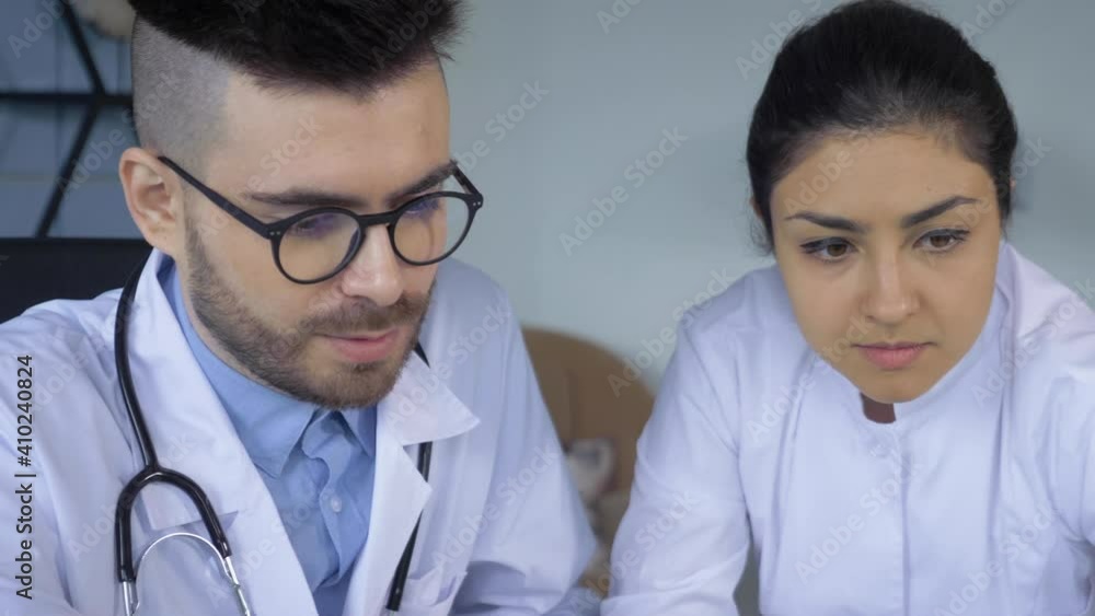 Close-up of Two doctors, a Man and a Woman, Looking at a Tablet screen or Working at a Computer or Laptop, Are in a Bright Hospital Office Close-up of Two doctors, a Man and a Woman, Looking at a Tablet screen or Working at a Computer or Laptop, Are in a Bright Hospital Office