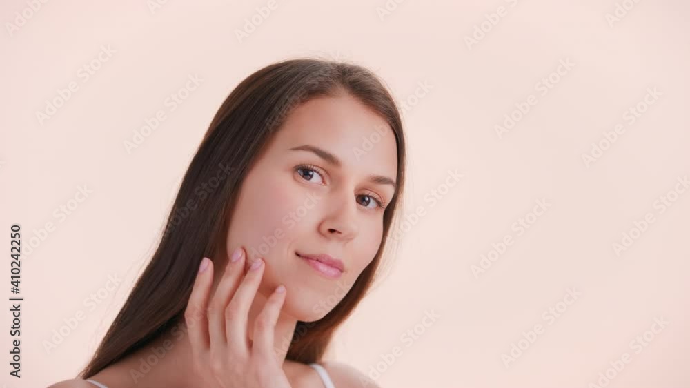 Beauty portrait of young brown-haired woman with perfect skin slowly touches her face sliding fingers from cheekbone down to the chin and looks at camera | Beauty products commercial concept Beauty portrait of young brown-haired woman with perfect skin slowly touches her face sliding fingers from cheekbone down to the chin and looks at camera | Beauty products commercial concept