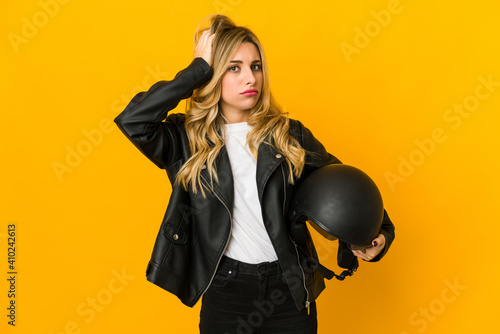 Young blonde caucasian biker woman holding helmet being shocked, she has remembered important meeting.