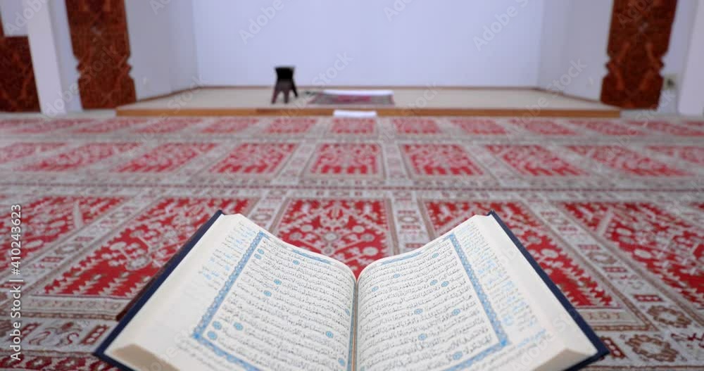 A Quran lying on a Quran holder, the shot moves from the Quran to the panel on the wall in the