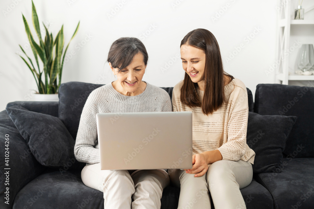 Two women diverse generations spend leisure time at home, a senior mother and an adult daughter is using a laptop. A young woman explains to mature woman how to use computer, helps to send email Two women diverse generations spend leisure time at home, a senior mother and an adult daughter is using a laptop. A young woman explains to mature woman how to use computer, helps to send email