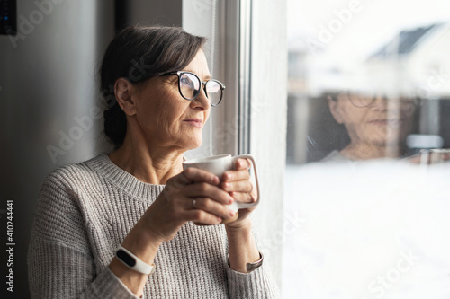 Fototapet Close-up portrait of senior older woman wearing glasses enjoys morning coffee in the kitchen at home