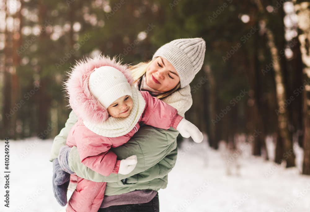 Young mother plays with her little daughter in winter in the park, holds in her arms and circles Young mother plays with her little daughter in winter in the park, holds in her arms and circles