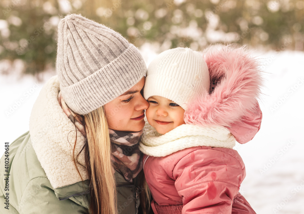 Young happy mother in winter holds her little daughter in her arms and looks at her. Family portrait. Motherhood and childhood Young happy mother in winter holds her little daughter in her arms and looks at her. Family portrait. Motherhood and childhood