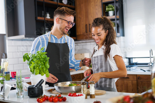 Young cheerful multi-ethnic couple preparing tomato pasta together at home kitchen