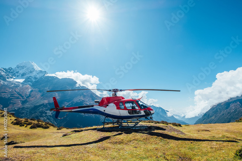 Civil helicopter landed in high altitude Himalayas mountains. Thamserku 6608m mountain on the background. Namche Bazaar, Nepal. Safety air transportation and travel insurance concept image. photo