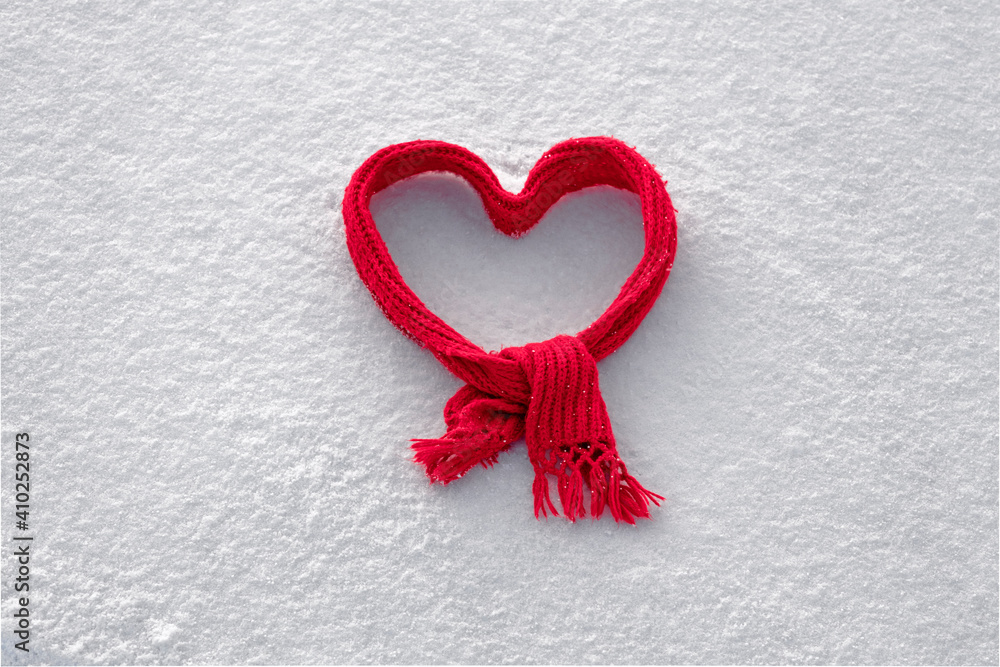 red knitted scarf folded in the shape of a heart on white snow, cute background for valentine's day