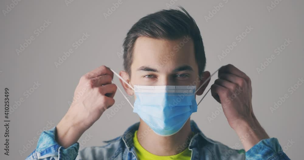 Young male removes the face protective mask and looking at the camera. Close-up portrait in studio. Virus, epidemic or pandemic concept. Young male removes the face protective mask and looking at the camera. Close-up portrait in studio. Virus, epidemic or pandemic concept.