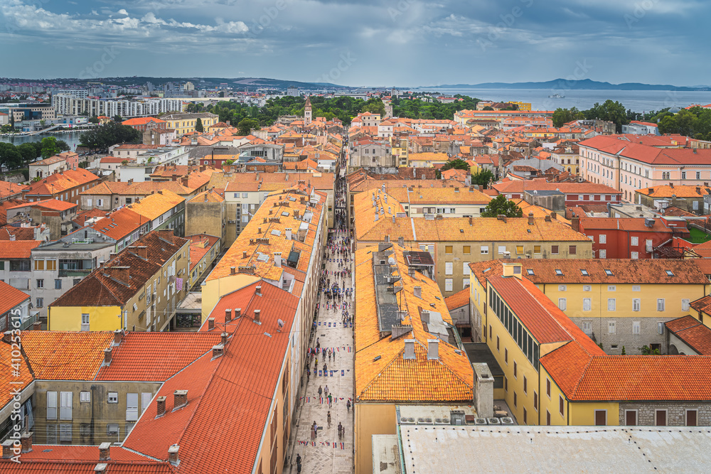 Drone or birds eye view on orange tiled roofs and cityscape of Zadar old town with bay. Tourists walking on beautiful stone alley, Croatia