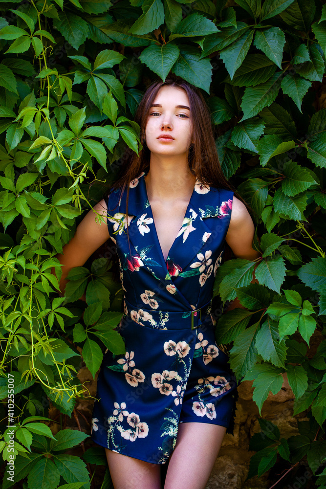 Young woman in blue flowers dress on green ivy background Young woman in blue flowers dress on green ivy background