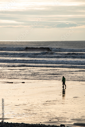 a man walking along the shoreline at borth beach 