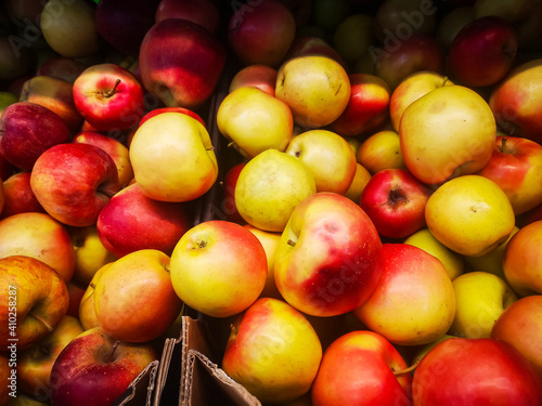 many red ripe apples lie on a shelf in a box in a supermarket