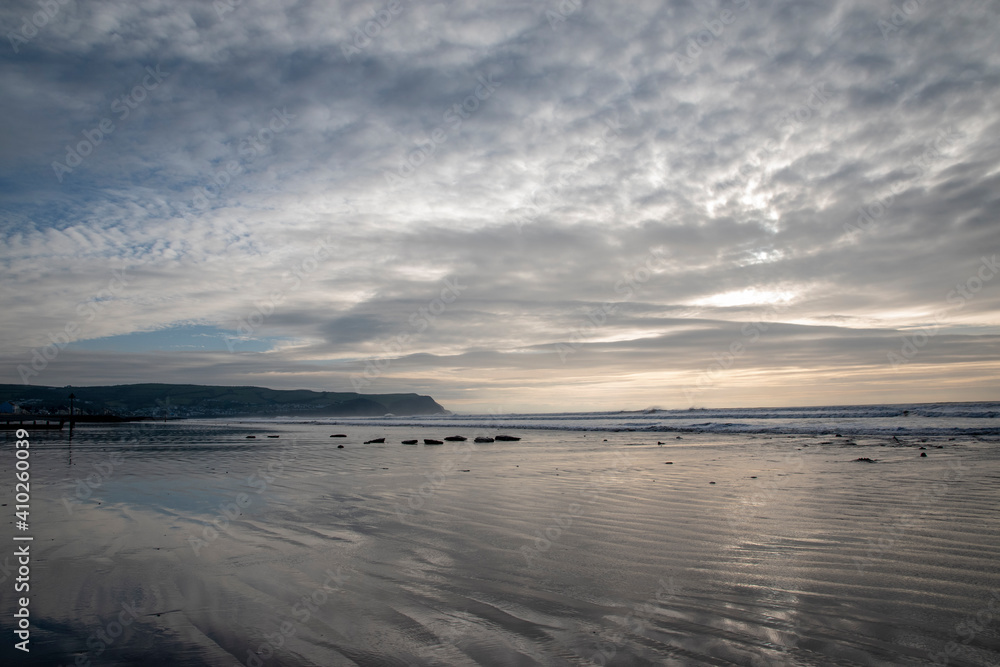 a long reflective beach with a row of stones leading into the sea a long reflective beach with a row of stones leading into the sea