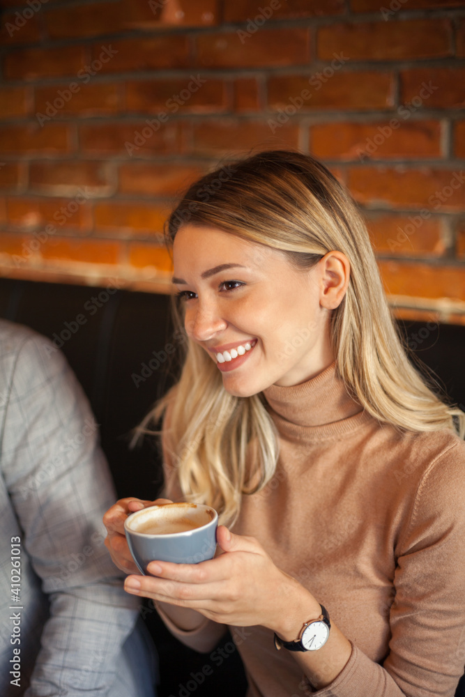 A pretty girl who sits with friends and listens carefully, while sitting in restaurant holding cup of coffee and smiling