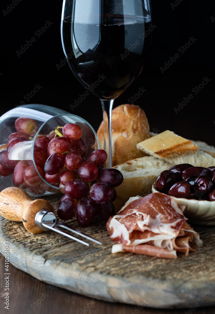 Close up of a rustic charcuterie board including prosciutto, bread and grapes with red wine. Close up of a rustic charcuterie board including prosciutto, bread and grapes with red wine.