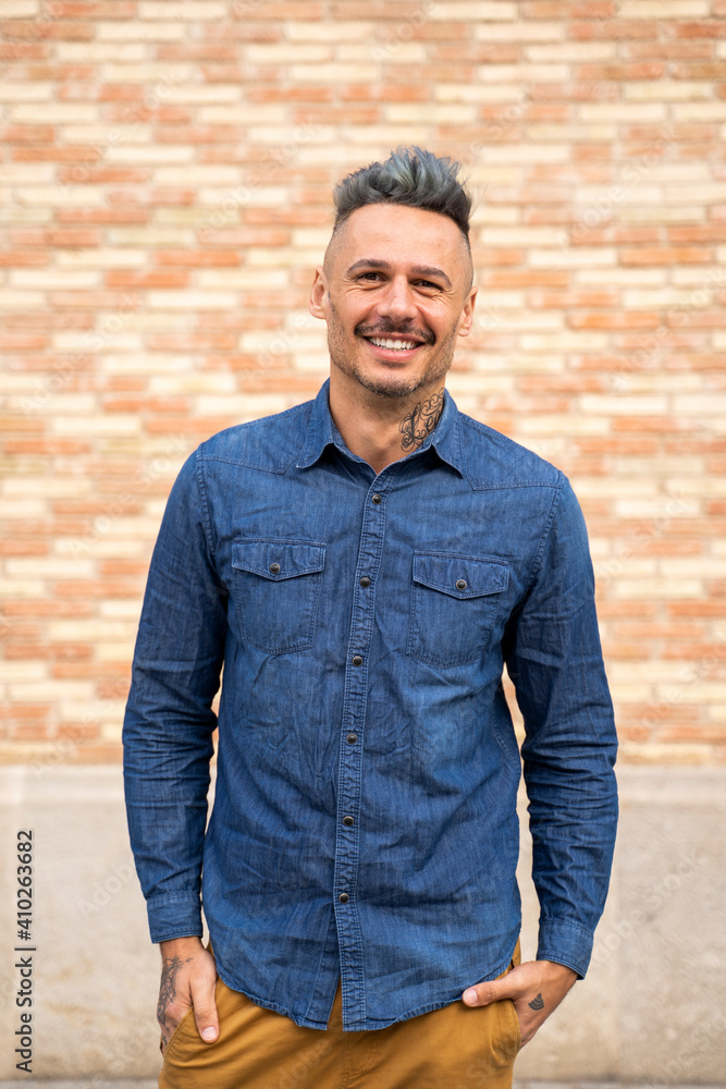 Smiling handsome man standing with hands in pockets against wall Smiling handsome man standing with hands in pockets against wall
