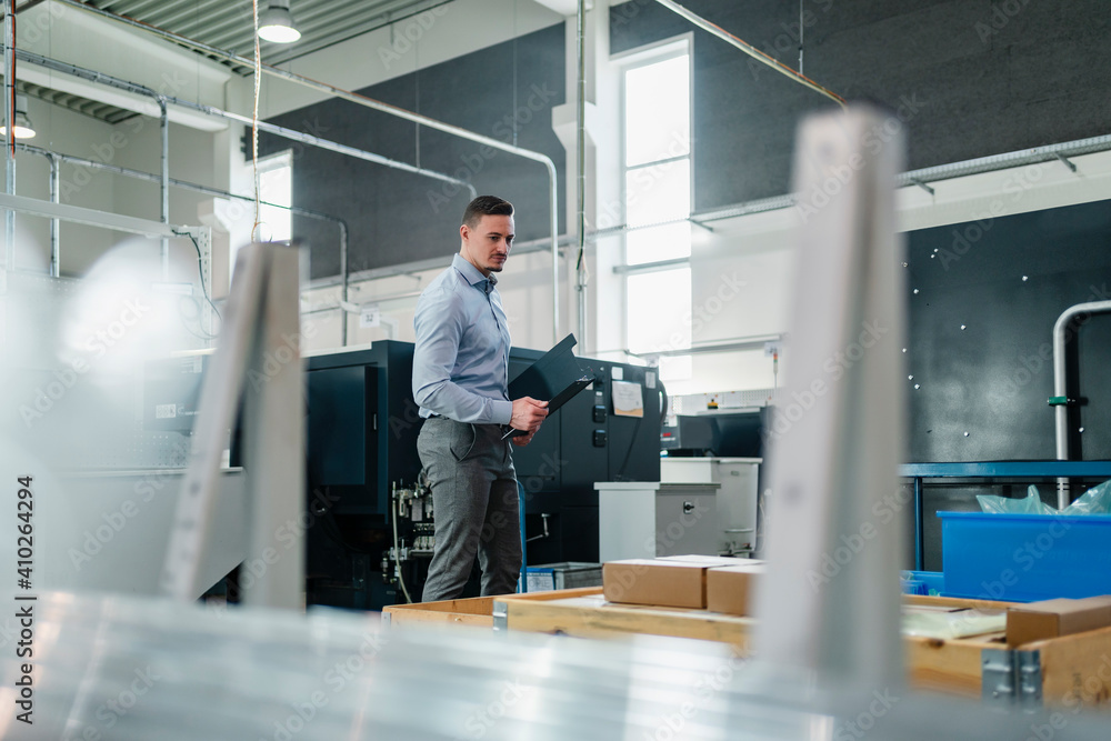 Mid adult businessman with file looking around at machinery in factory Mid adult businessman with file looking around at machinery in factory