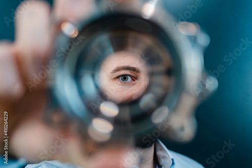 Male professional's eyes seen through circular machine part in factory