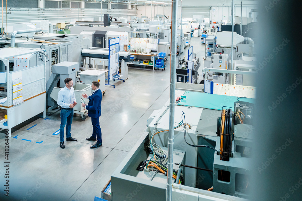 Businessman with male colleague discussing over digital tablet by machinery equipment Businessman with male colleague discussing over digital tablet by machinery equipment