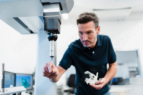 Male engineer with machine part adjusting drill bit in equipment at industry office