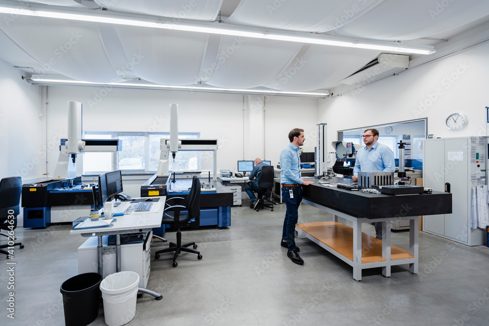 © Daniel Ingold/Westend61 - Engineers talking while standing in measuring room at office