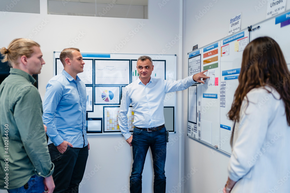 Businessman explaining plan to coworker standing in meeting at office Businessman explaining plan to coworker standing in meeting at office