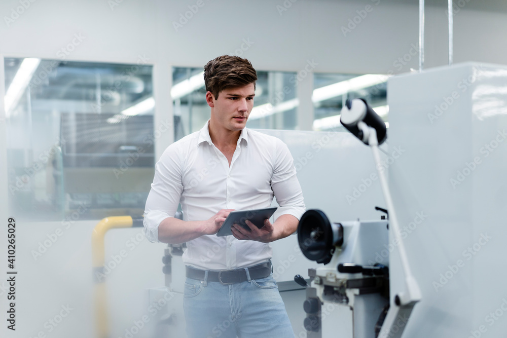 Young businessman holding digital tablet while examining machines in industry Young businessman holding digital tablet while examining machines in industry