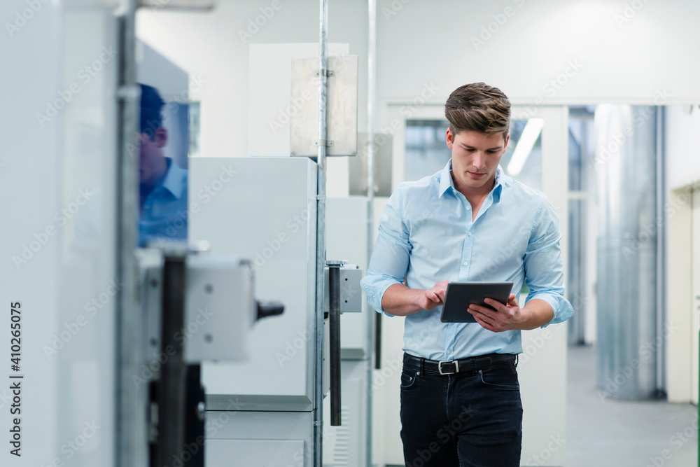 Male entrepreneur working on digital tablet while walking by machines in factory Male entrepreneur working on digital tablet while walking by machines in factory