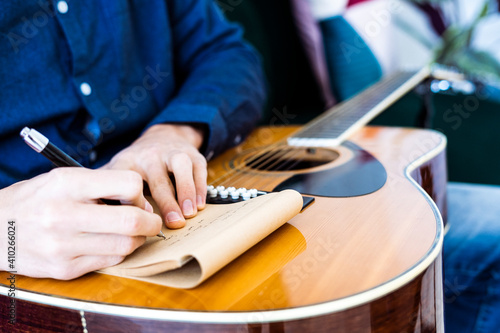 Song writer writing music on note pad while sitting with guitar at studio photo