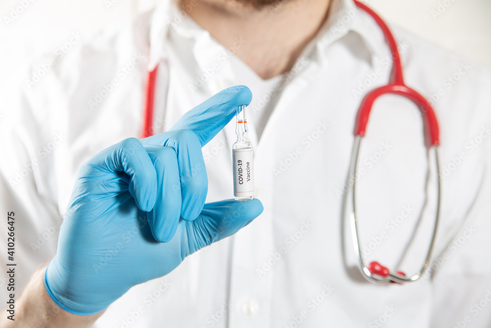 A medical worker hand in protective glove holding COVID-19 vaccine bottle. A medical worker hand in protective glove holding COVID-19 vaccine bottle.