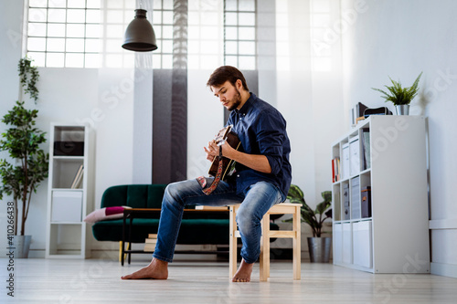 Professional doing rehearsal with guitar while sitting on stool at studio photo