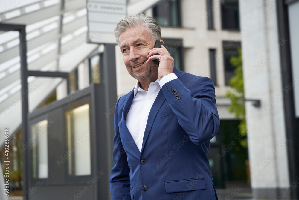 Smiling businessman talking on mobile phone while waiting at bus stop in city Smiling businessman talking on mobile phone while waiting at bus stop in city