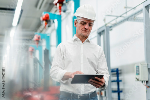 Mature male technician wearing hardhat working in digital tablet in industry photo