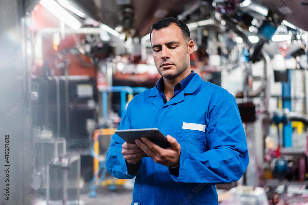 Engineer in blue coat working on digital tablet in factory Engineer in blue coat working on digital tablet in factory