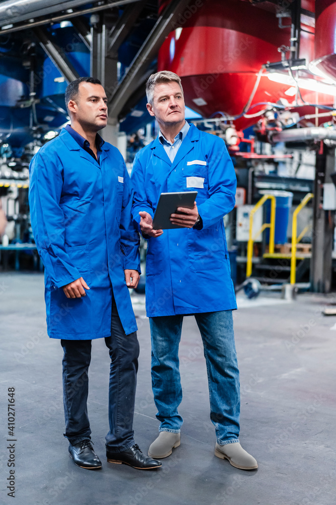 Mature male colleagues with digital tablet looking away while standing in industry Mature male colleagues with digital tablet looking away while standing in industry