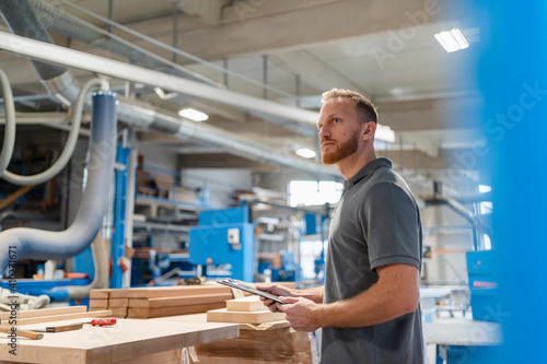 Portrait of carpenter standing in production hall with clipboard in hands