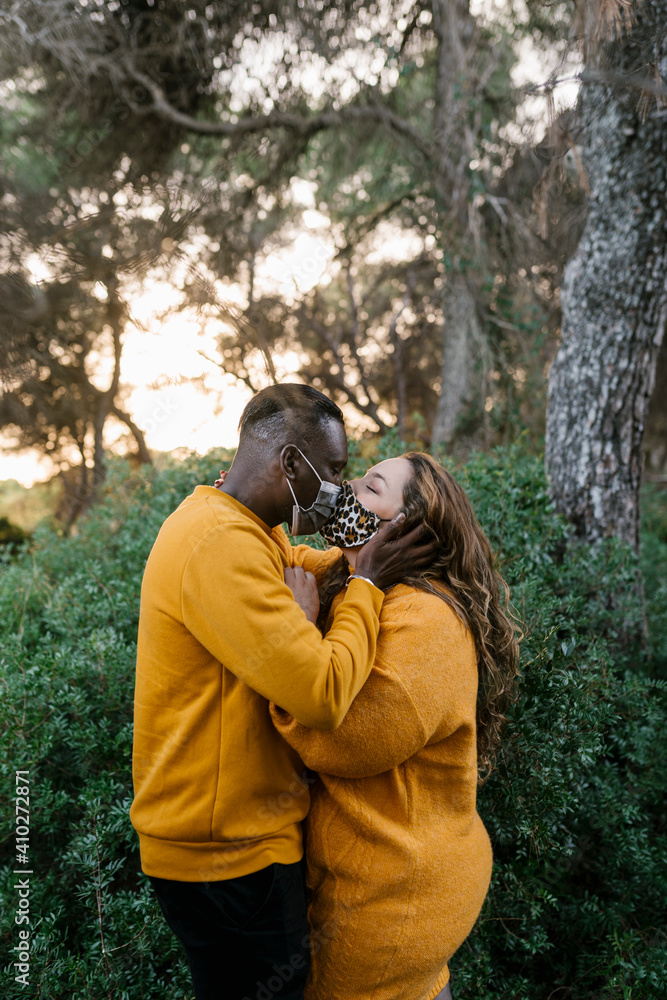 Man wearing face mask kissing woman while standing at forest Man wearing face mask kissing woman while standing at forest