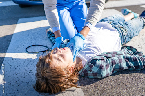 Doctor checking unconscious boy lying on road after car accident photo