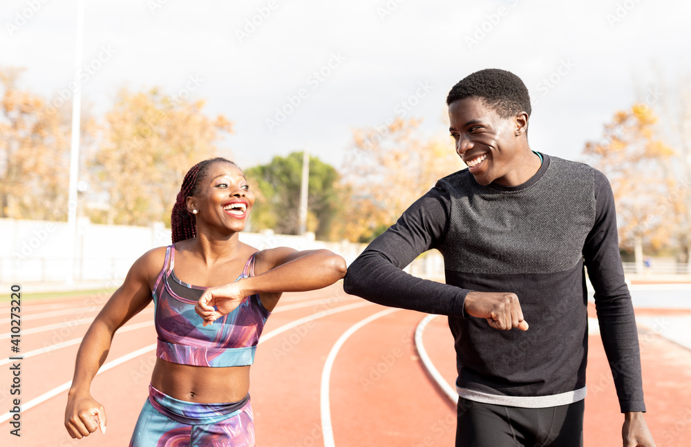 Male and female athlete doing elbow bump while walking on track during sunny day Male and female athlete doing elbow bump while walking on track during sunny day