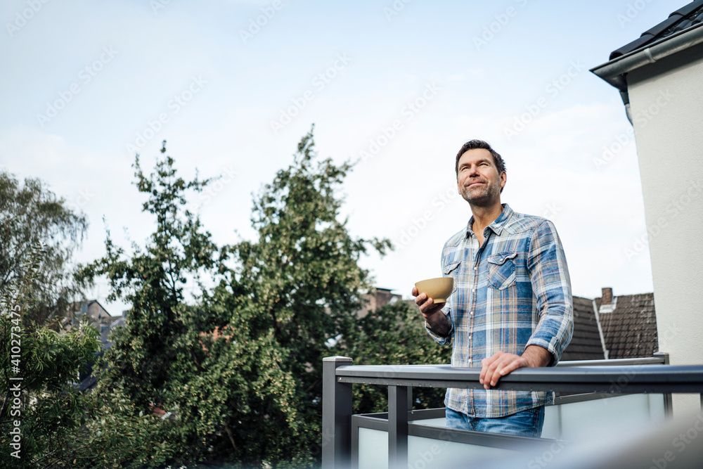 Mature man day dreaming while holding bowl in balcony of house