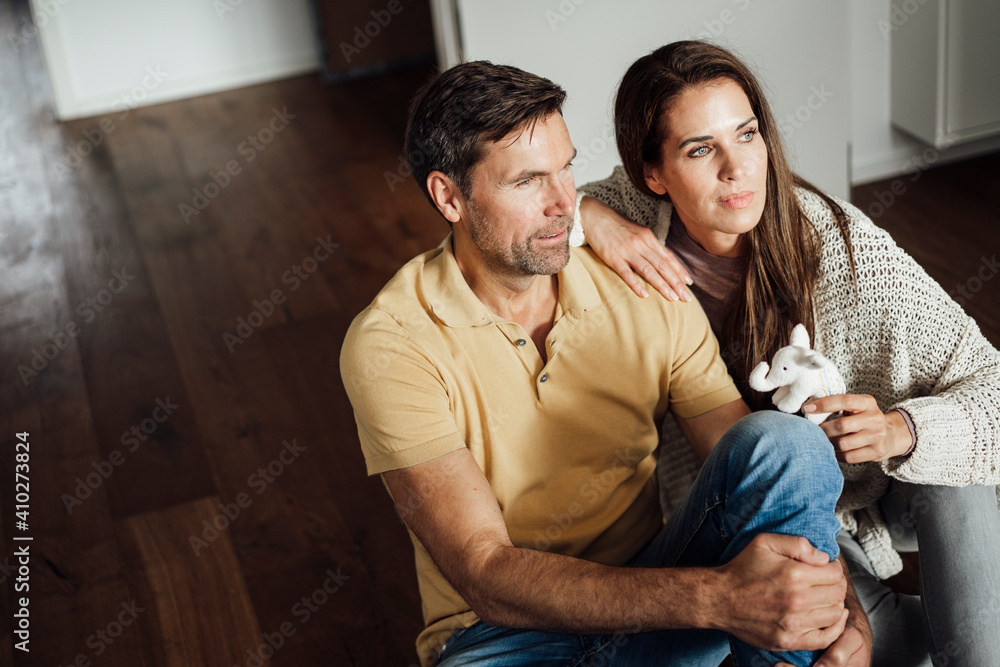 Mature woman holding elephant stuffed toy while day dreaming with man in apartment Mature woman holding elephant stuffed toy while day dreaming with man in apartment