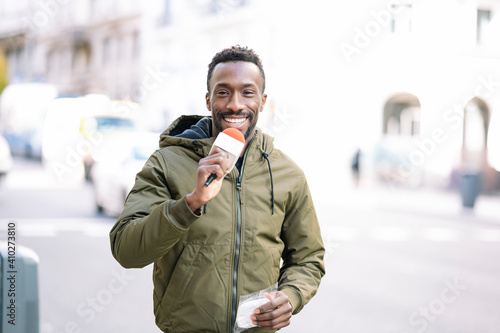 Smiling male journalist with microphone standing on street in city photo