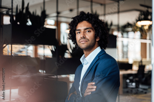 Confident handsome young male professional standing with arms crossed at office