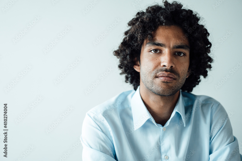 Confident young businessman with curly black hair against white wall in office Confident young businessman with curly black hair against white wall in office
