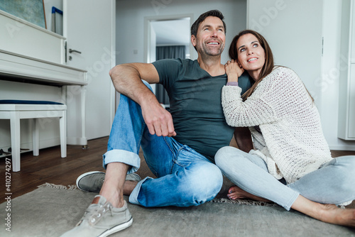 Smiling mature couple day dreaming while sitting on floor at home photo