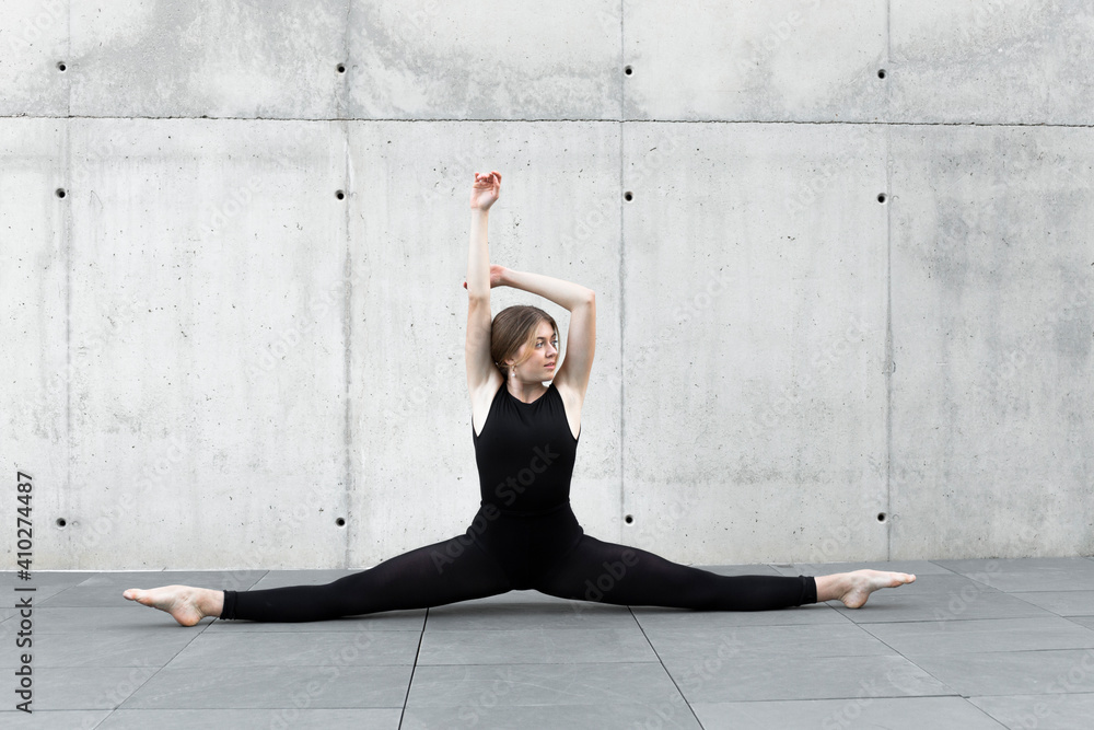 Dancer in black leotard doing split in front of concrete wall