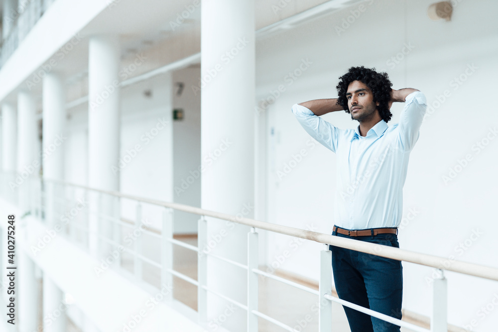 Young male entrepreneur with hands behind head looking away while contemplating in corridor at office
