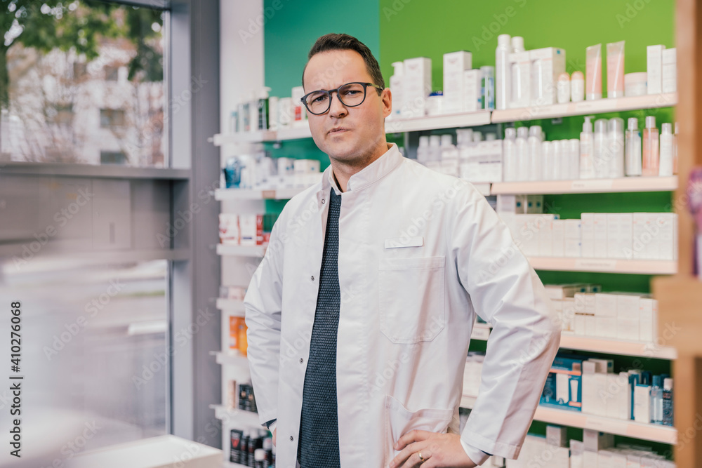 Contemplating pharmacist wearing lab coat while standing in chemist shop Contemplating pharmacist wearing lab coat while standing in chemist shop