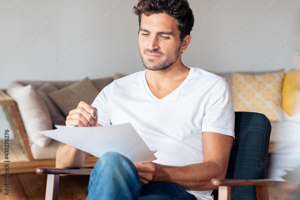 Man concentrating on paper while sitting on armchair at home Man concentrating on paper while sitting on armchair at home